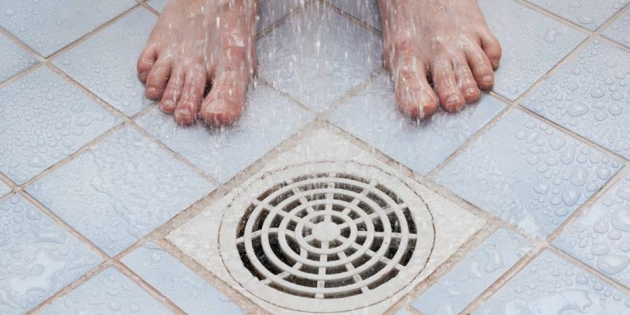 Close-up of shower drain with someone standing beside it